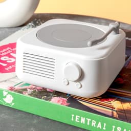 A white Bluetooth speaker designed to resemble a vintage record player, placed on top of a colourful magazine.