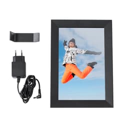A black digital photo frame with a charging cable and stand, displaying a joyful person in bright orange pants against a blue sky.