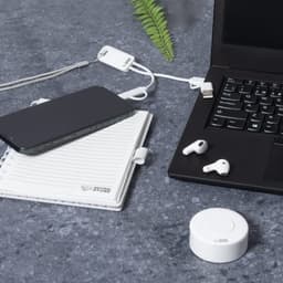A set of white earbuds rests beside a black smartphone, notebook, and laptop on a grey surface.