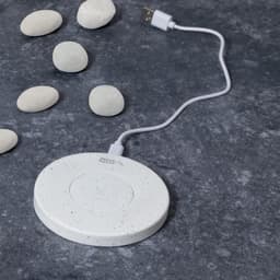 A white wireless charger with a speckled finish, accompanied by smooth pebbles on a dark surface.