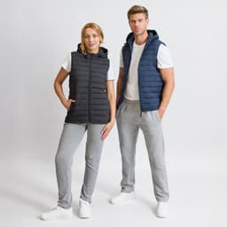 A black and navy puffer vest with a hood is displayed on two models, paired with casual grey pants and white sneakers.