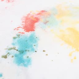 A women's T-shirt in white featuring a colourful splash design in red, blue, yellow, and green. Includes a logo.