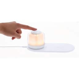 A white wireless charger with a glowing, translucent dome on top, being touched by a hand.