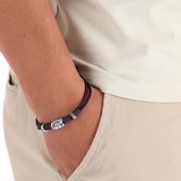 A brown leather bracelet with metal accents worn on a wrist, partially tucked into a pocket.