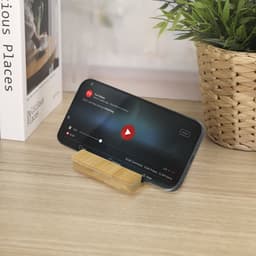 A phone stand in a natural wood finish supports a smartphone displaying a video playback screen against a light wooden surface.