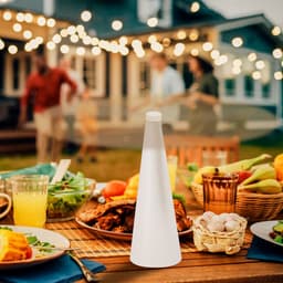 A white fly repellent fan positioned on a table set with food and drinks, with a festive outdoor backdrop.