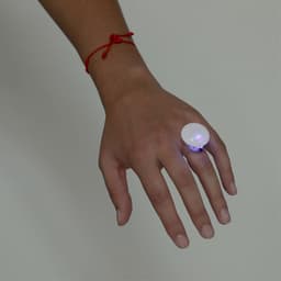 A light-up novelty ring with a large round white top, worn on a hand with a red string bracelet.