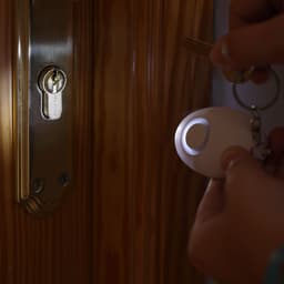 A keychain flashlight with a white body illuminates a door lock as keys are inserted.
