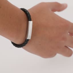 A black braided leather bracelet with a silver metal clasp displayed on a wrist.