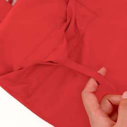 A red rain jacket with an inner pocket detail and a hand gesturing toward it. Features a branding logo.