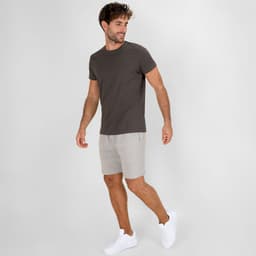 A man wears light grey dress shorts paired with a dark grey t-shirt and white sneakers. The image features branding.