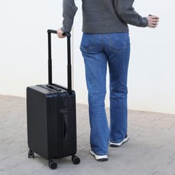 A wheeled black bag is being pulled by a person wearing grey and blue jeans, with a casual stance.