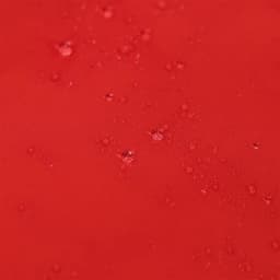 A close-up of a red puffer jacket fabric displaying water droplets and texture. Features branding.