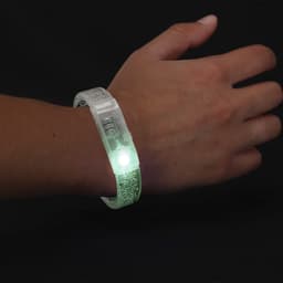 A glow-in-the-dark wristband with a textured design, illuminating with a bright white light. Features a logo.