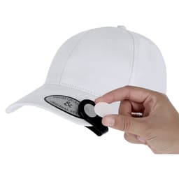 A hand holds a white circular ball marker next to a white cap featuring a logo.