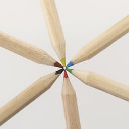 A collection of coloured pencils with red, blue, green, yellow, black, and brown tips arranged in a circular pattern.