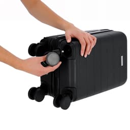 A black wheeled bag with a person adjusting the handle and wheels. The bag features a logo on its surface.