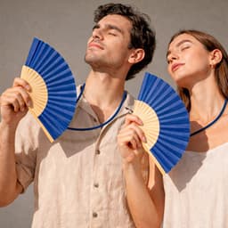 Two people holding blue handheld fans with wooden handles, wearing casual, light-coloured clothing.