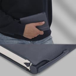 A dark grey notebook held against a person's side, featuring a sleek design and metallic clip.