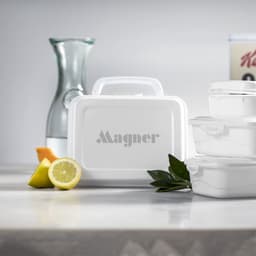 A white lunch box with a handle, surrounded by lemon, orange slices, and glassware. It features a logo on the front.