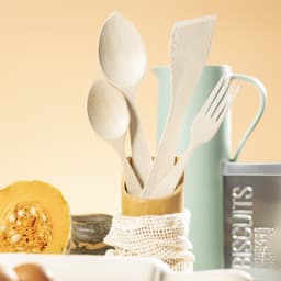 A set of bamboo cooking utensils including spoons, a spatula, and a fork, in a bamboo holder with decorative items.