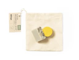 A set of handmade soap bars in various colours, including yellow and white, packaged in a natural fabric pouch.