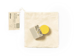 A set of two soap bars, one white with herbs and one yellow, packaged in a natural cotton pouch.