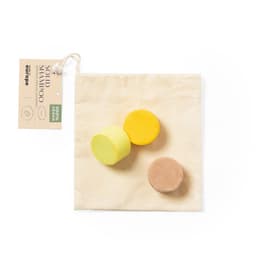 Three solid shampoo bars in yellow, brown, and light yellow, placed in a natural fabric pouch. The pouch has a brand tag.