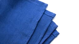 A blue fabric placemat with textured surface and folded edges, featuring a branding logo.