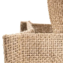 A natural jute bag with textured woven fabric and sturdy handles. The bag features a simple design and a rustic look.