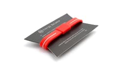 A red Energy Bracelet displayed on a black card, featuring white stripes and a logo.