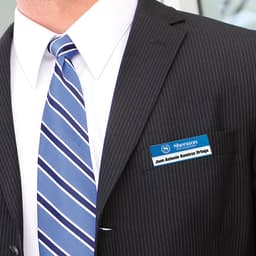 A name badge displayed on a formal suit, featuring a blue and white design with a logo.