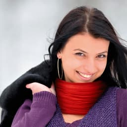 A smiling woman wears a red scarf and a dark coat, set against a snowy background.