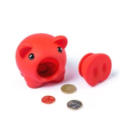 A red piggy bank with a slot for coins and a removable base, accompanied by several coins on a white surface.