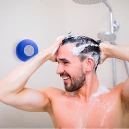 A blue Bluetooth speaker mounted on a wall, with a man washing his hair in the shower.