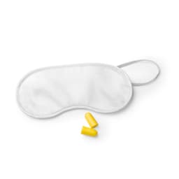 A white sleeping mask with two yellow earplugs placed beside it. The mask has an adjustable strap and a logo.