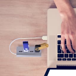 A USB hub features multiple drives in blue, black, and gold connected to a laptop on a wooden surface.