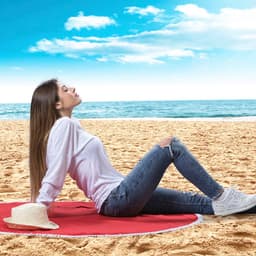 A picnic rug in a vibrant red hue, with a woman in casual clothing reclining on a sandy beach.