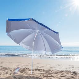A beach umbrella with a light grey canopy and blue trim, set on sandy beach with ocean waves in the background.