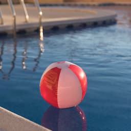 A red and white inflatable beach ball floats on the surface of a swimming pool.