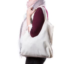 A cream tote bag is being held by a person wearing a scarf, showcasing its spacious design and simplicity.