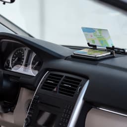 A car dashboard featuring a phone holder, displaying a phone with a map and a credit card on top.