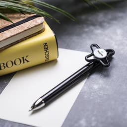 A black pen with a unique clip design rests on a blank notepad and a yellow notebook, accompanied by a plant.