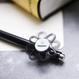 A black Karsol pen with a flower-shaped grip sits beside a notebook and a yellow book, featuring a branding logo.