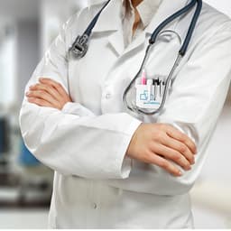 A doctor in a white lab coat with crossed arms, wearing a stethoscope and holding pens in the pocket.