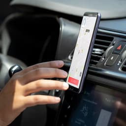 A phone stand in a car, securely holding a smartphone displaying a map. The stand has a sleek design and a dark colour.
