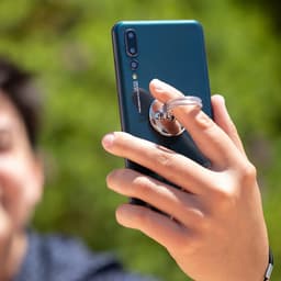 A green smartphone with a circular phone stand attached, being held by a hand against a natural background.