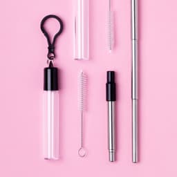 A set of stainless steel drinking straws in various lengths, accompanied by a cleaning brush and a carrying case, on a pink background.