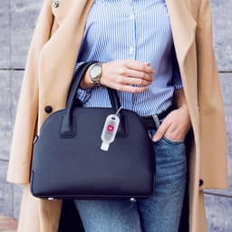A black handbag held by a person wearing a beige coat and blue striped shirt, with a silver watch on their wrist.