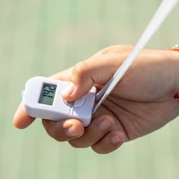 A white digital tally counter held in a hand, featuring a clear display and a strap.